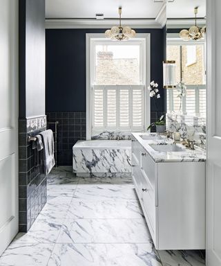 An example of how to design a bathroom showing a bathroom with large marble floor tiles and black walls, and a marble bath below a window