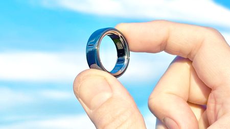 Close-up of the Oura Ring 4 Ceramic shining in the sunlight in a user's hand with blue skies and clouds behind it