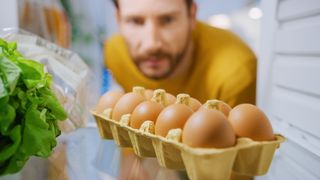 Someone looking at a carton of eggs from within a fridge