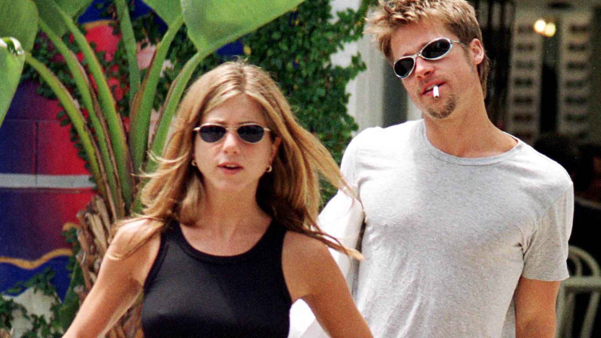 Image of Jennifer Aniston from 1999 wearing a black tank top with red trousers and black flip flops.