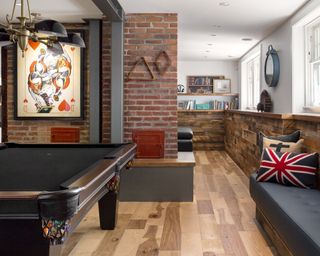 Basement with wood floor, brick partition wall, wood paneling to half height and white painted walls above, and built-in bench seating