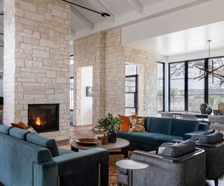 living room with blue sofas and low round coffee table with gray lounge chairs and fire lit