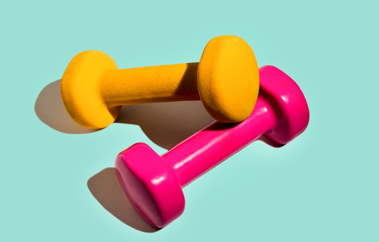 Fitness equipment pink yellow dumbbells on pastel mint green background. Sport lifestyle concept with dumbbells for home exercise. Copy space. Front view. Best dumbbells for women