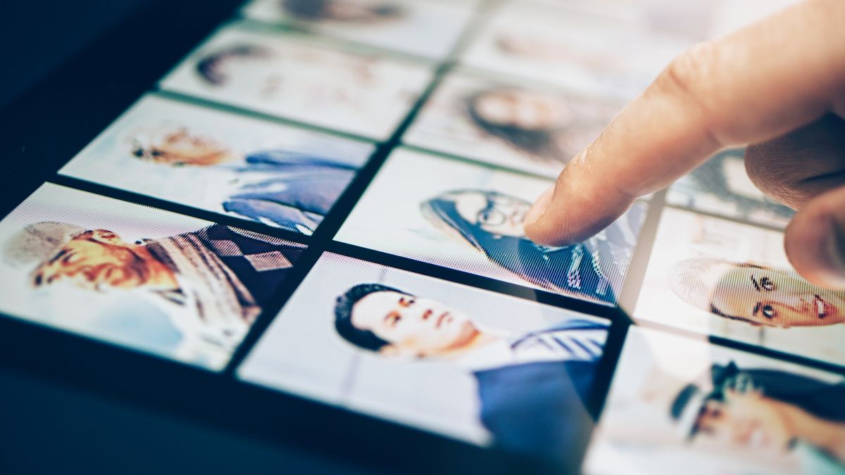 A close up of a tablet screen showing a series of headshots of potential applicants, with a finger pointing to one in the middle