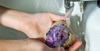 hands holding a amethyst stone under running water to show how to cleanse crystals
