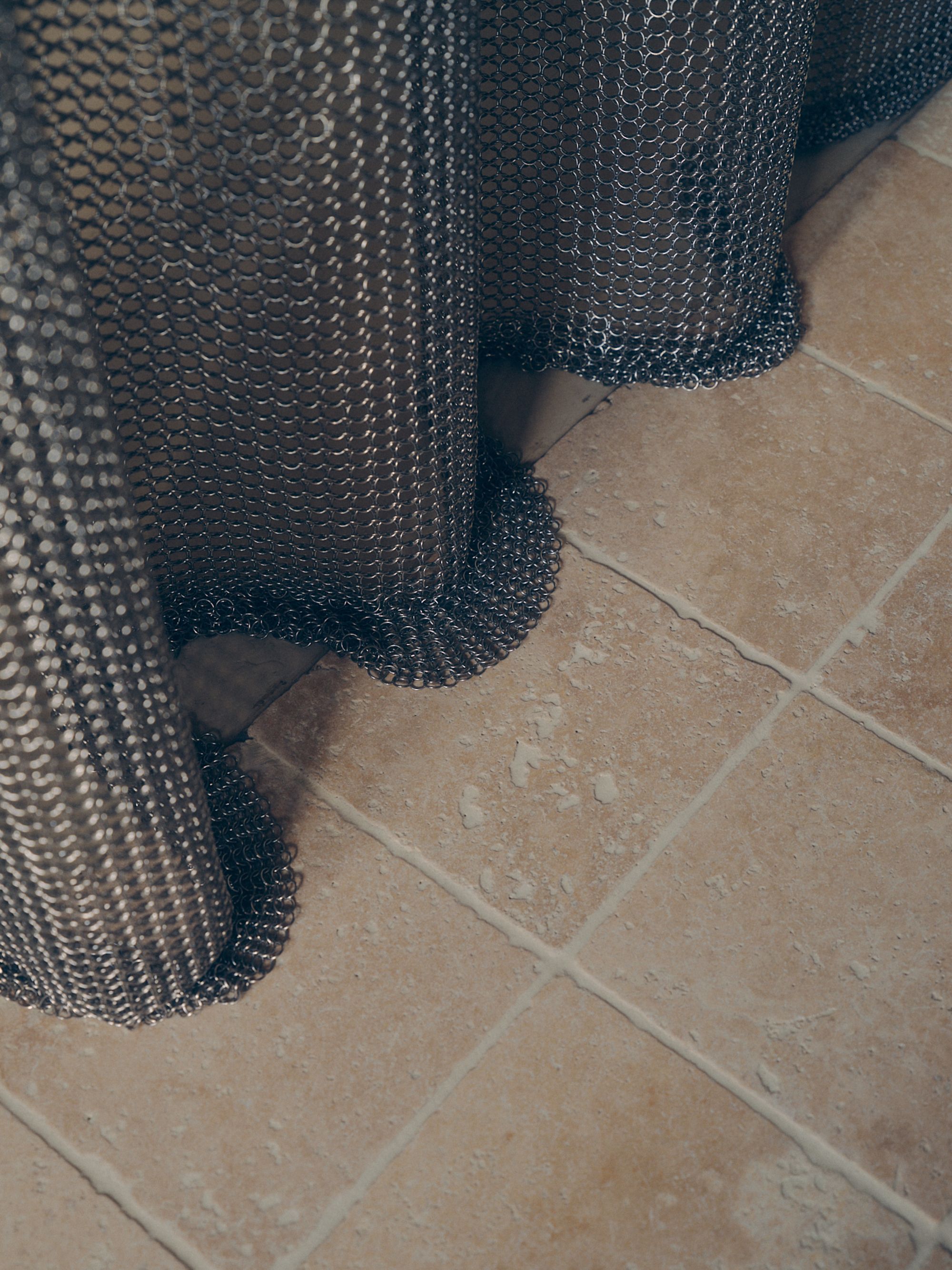 close up of chainmail shower curtain against tumbled floor tiles