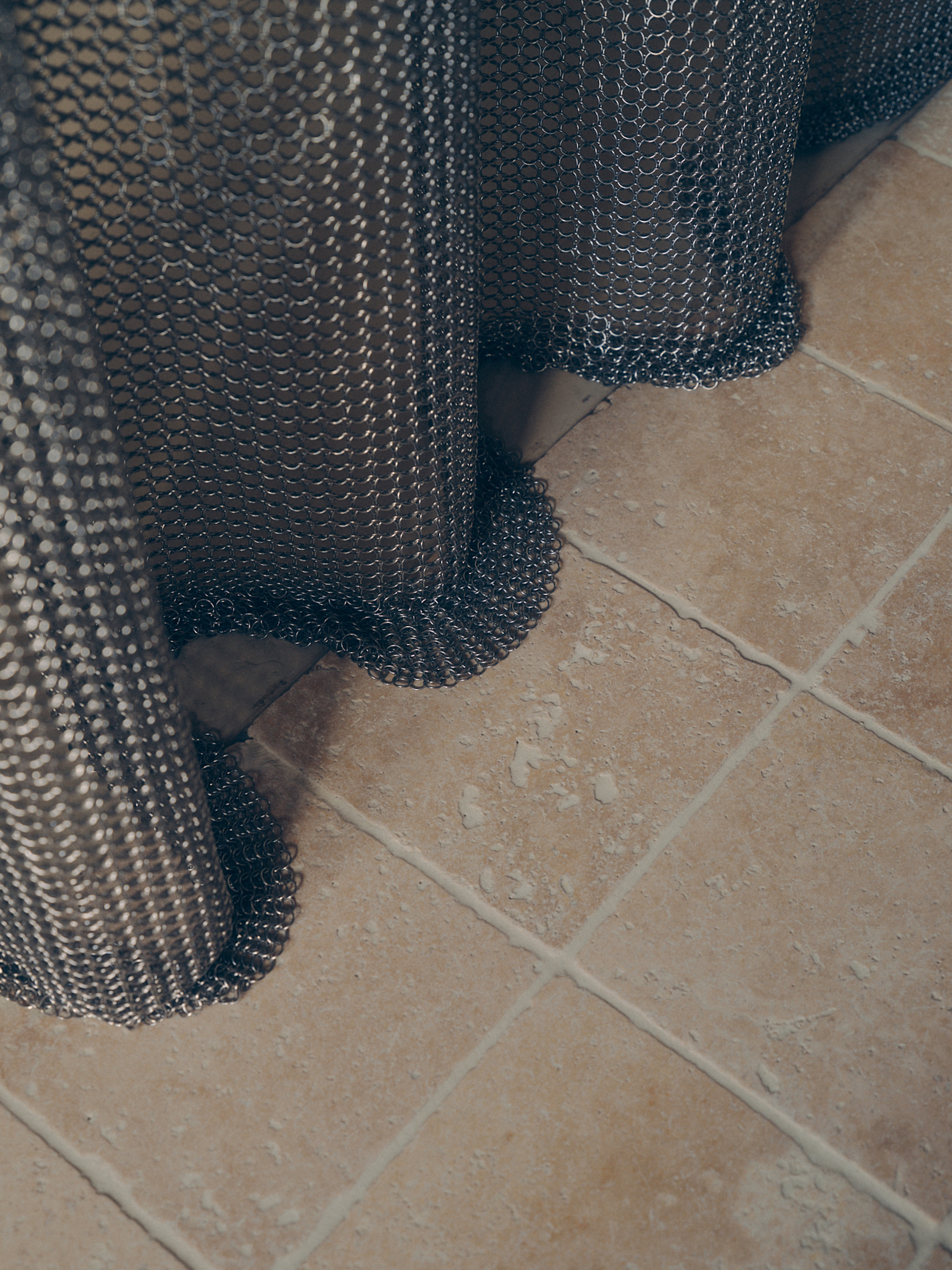 close up of chainmail shower curtain against tumbled floor tiles