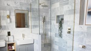 a gray and gold bathroom, with a tiled shower, sink and gold fixtures such as a mirror and lighting