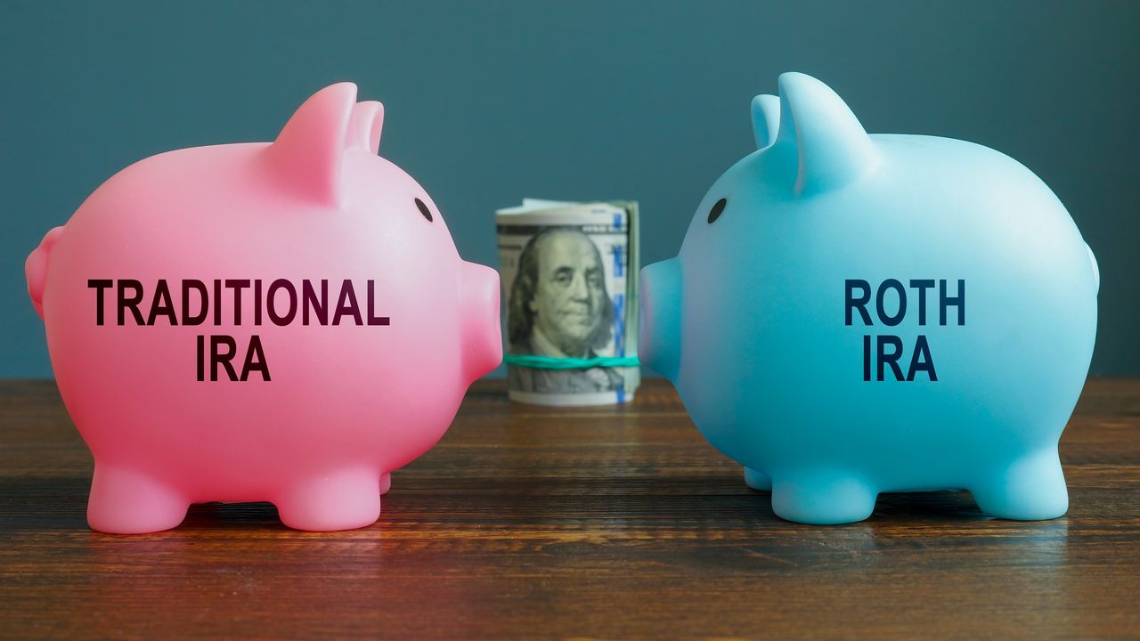 Piggy banks with &quot;traditional IRA&quot; and &quot;Roth IRA&quot; written on them face each other with a roll of cash between them.