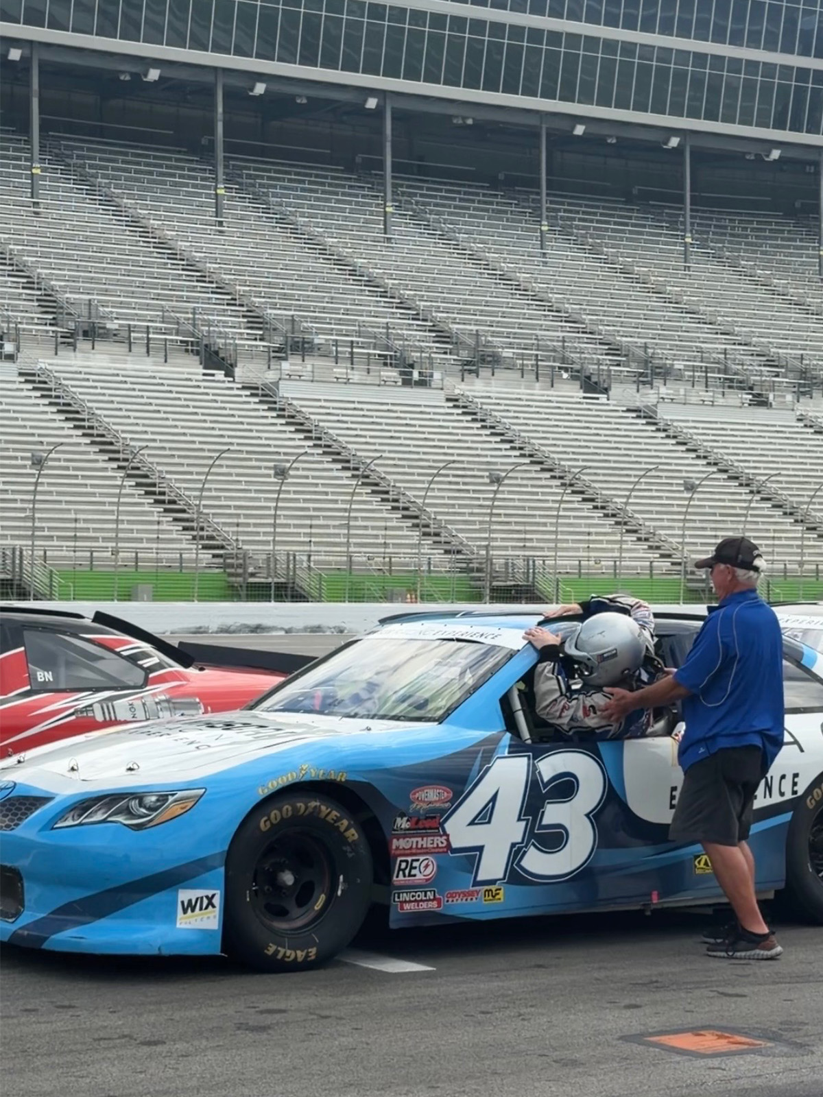 Chase Stokes getting help out of a blue race car with the number 43 on it.