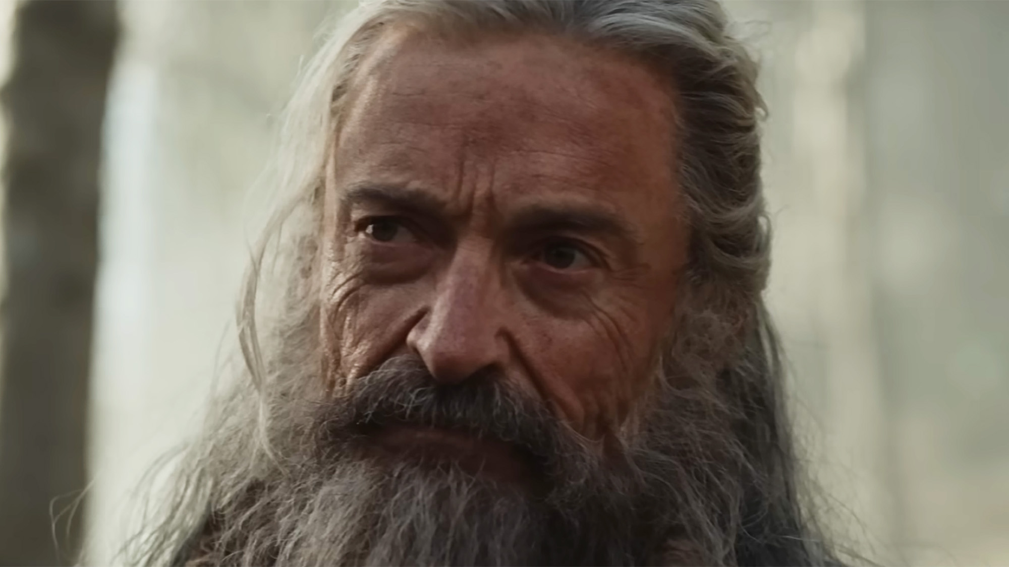 Hugh Jackman with grey wig and beard looking grizzled in A24's The Death Of Robin Hood. 