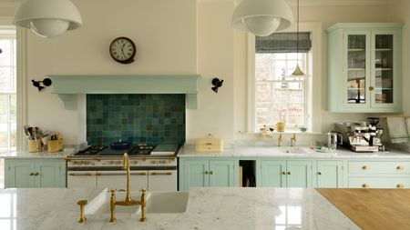 off white and pale green kitchen with tiled backsplash, marble countertops, sink in island, white stove, white pendant lights and glazed wall cabinet, coffee maker, black wall lights 