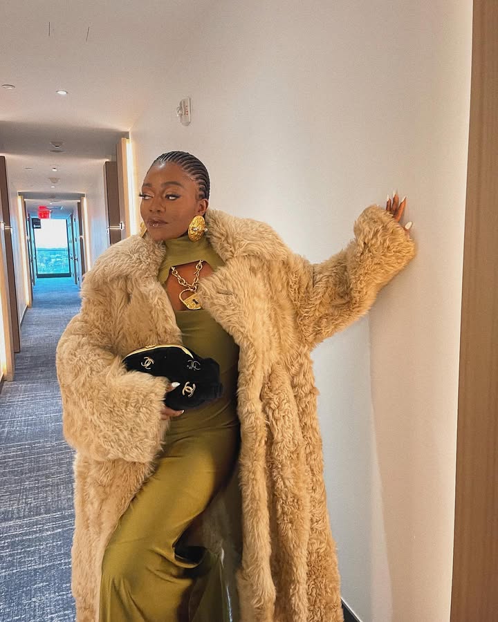 A woman wears gold jewelry, a gold dress, and a black chanel bag.