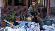 An Israeli soldier with a gun by a destroyed house 