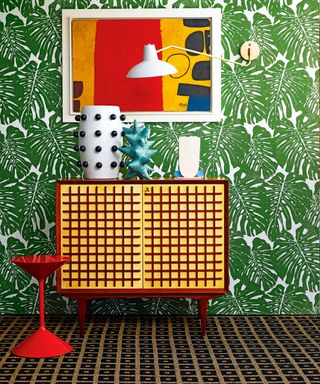 A brightly colored mid-century modern living room with abstract art and palm leaf print wallpaper.