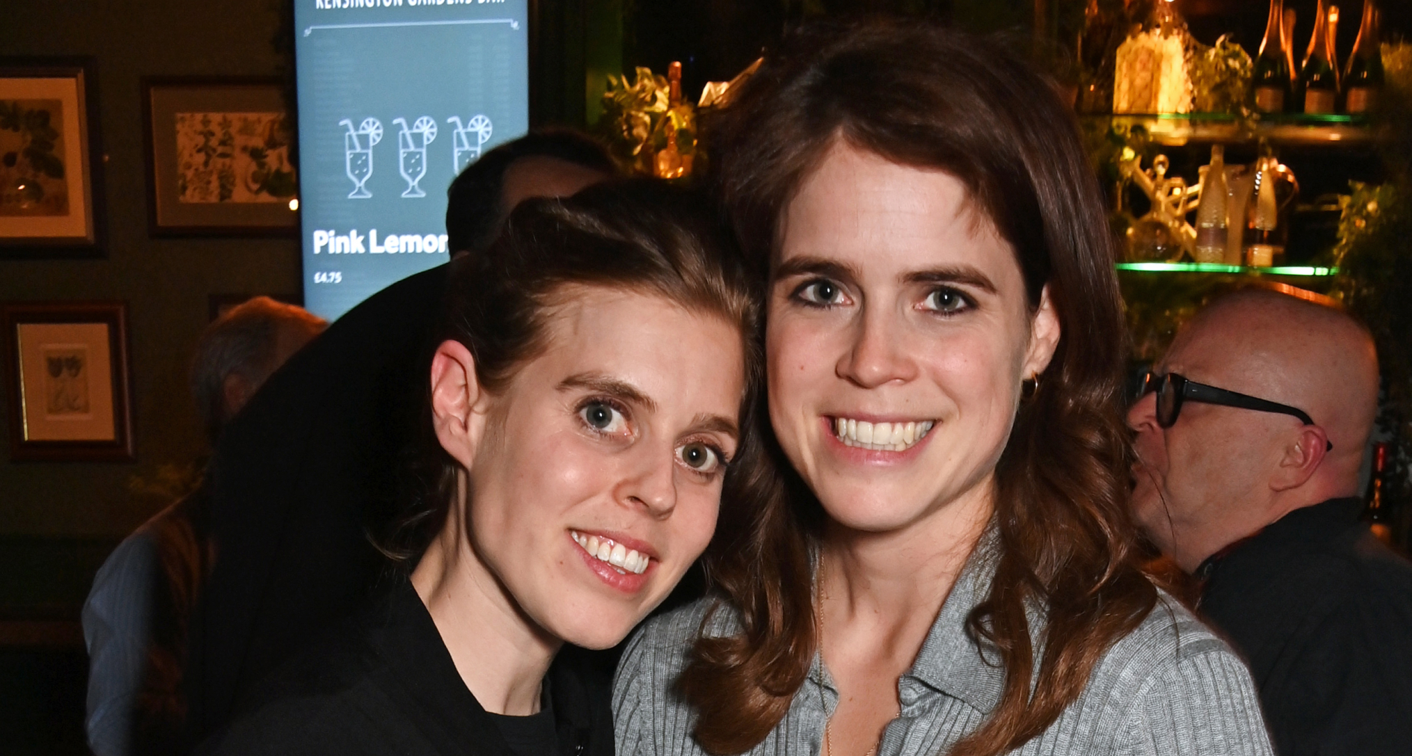 Princess Beatrice and Princess Eugenie smiling in a bar
