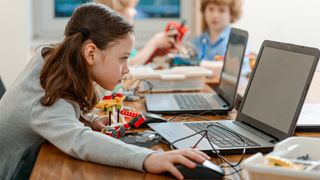 A schoolgirl using a laptop to program a robot made of plastic bricks
