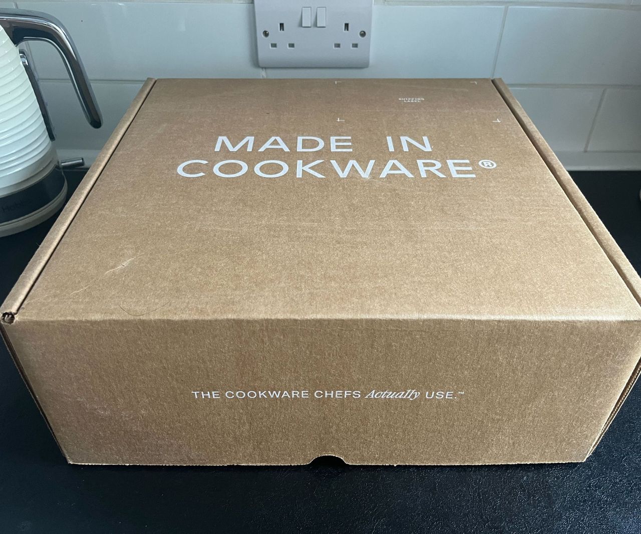 A Made In cookware cardboard box on a black kitchen counter.