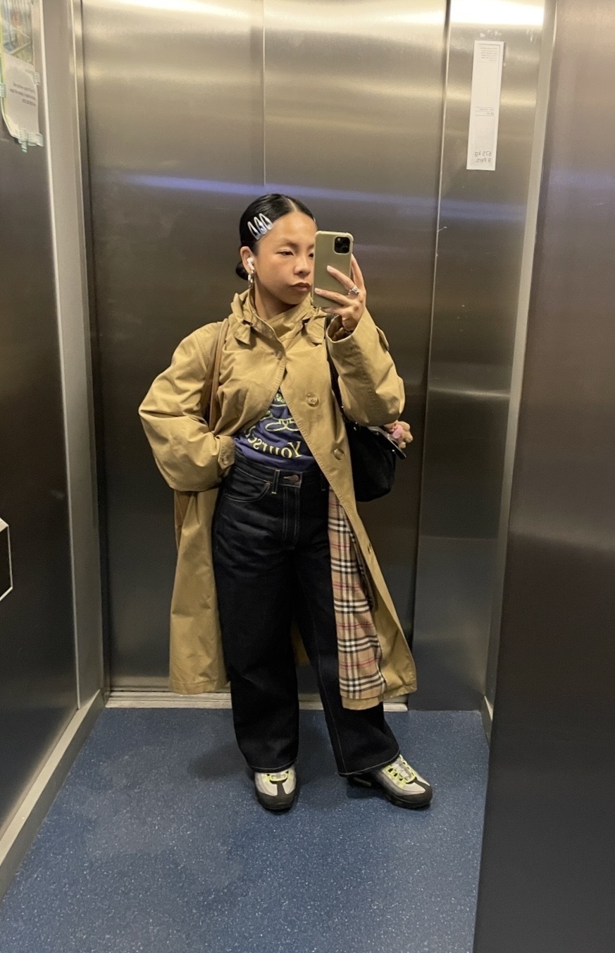 Woman wears Burberry trench coat, graphic Tee, blue jeans and trainers