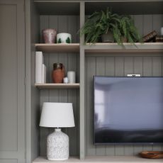 TV mounted on panelled media wall with shelving, decorated with table lamps, vases, and books