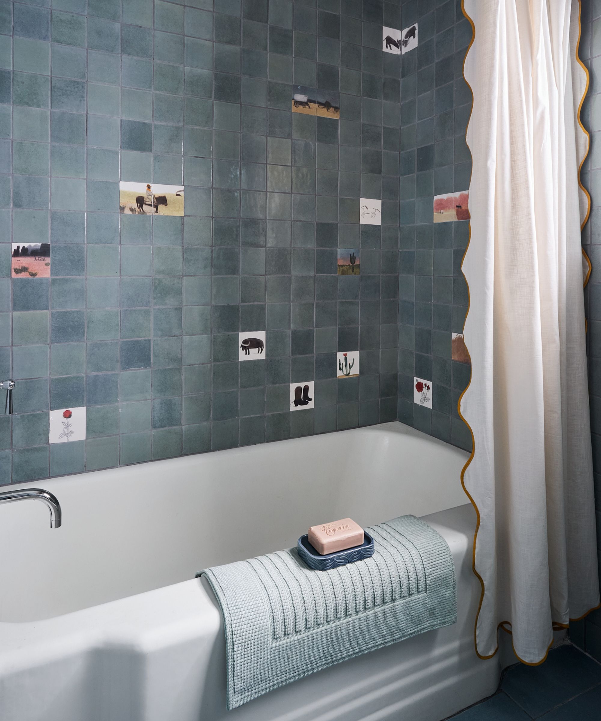 a blue zellige tiled bath shower with hand painted cowboy themed tiles and a scalloped shower curtain