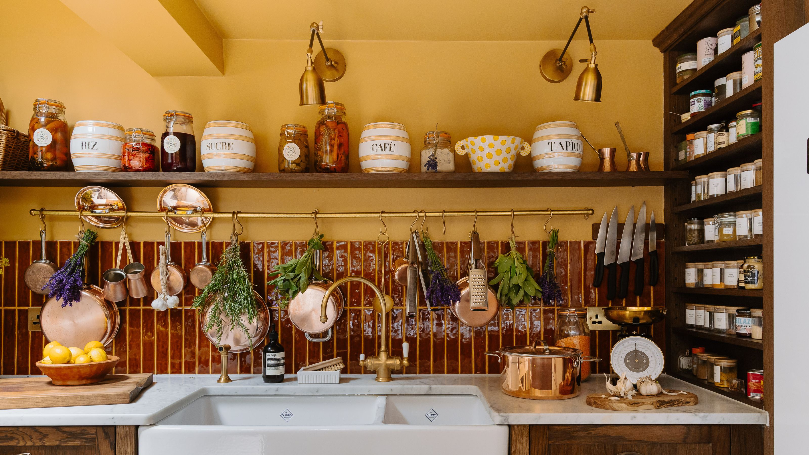 Clodagh McKenna's kitchen featuring yellow walls, burgundy tiles, wooden open shelving, and collected decor