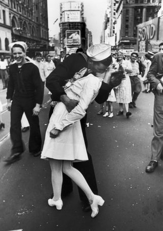 A jubilant American sailor clutching a white-uniformed nurse in a back-bending, passionate kiss as he vents his joy while thousands jam Times Square to celebrate the long awaited-victory over Japan. This photo — perhaps the most famous picture in history of a kiss — was taken by Alfred Eisenstaedt.