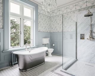 A bathroom with chandelier, freestanding bath and blue and white wallpaper