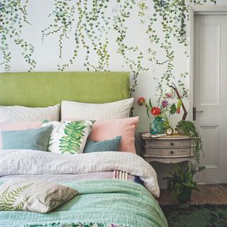 how to decorate a guest bedroom, botanical bedroom with green bed, green and pale pink bedding, vintage side table, plants, trailing leaf wallpaper, wooden floor, rug