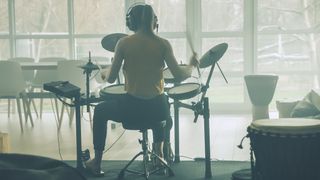 Women wearing a yellow top plays an electronic drum set in a room with large windows