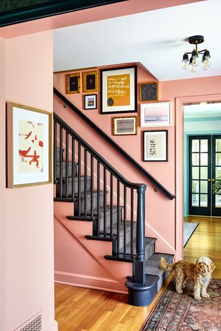 pink entryway with black stair rail and black frames on the art up the wall