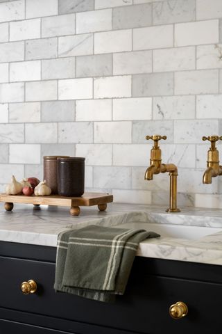 A kitchen sink with two traditional style brushed brass faucets and a marble countertop
