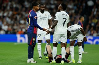 Barcelona's Spanish forward #19 Lamine Yamal (L) talks with Real Madrid's Brazilian forward #07 Vinicius Junior as Barcelona's Polish forward #09 Robert Lewandowski lies on the field during the Spanish league football match between Real Madrid CF and FC Barcelona at the Santiago Bernabeu stadium in Madrid on October 26, 2024. (Photo by OSCAR DEL POZO / AFP) (Photo by OSCAR DEL POZO/AFP via Getty Images)