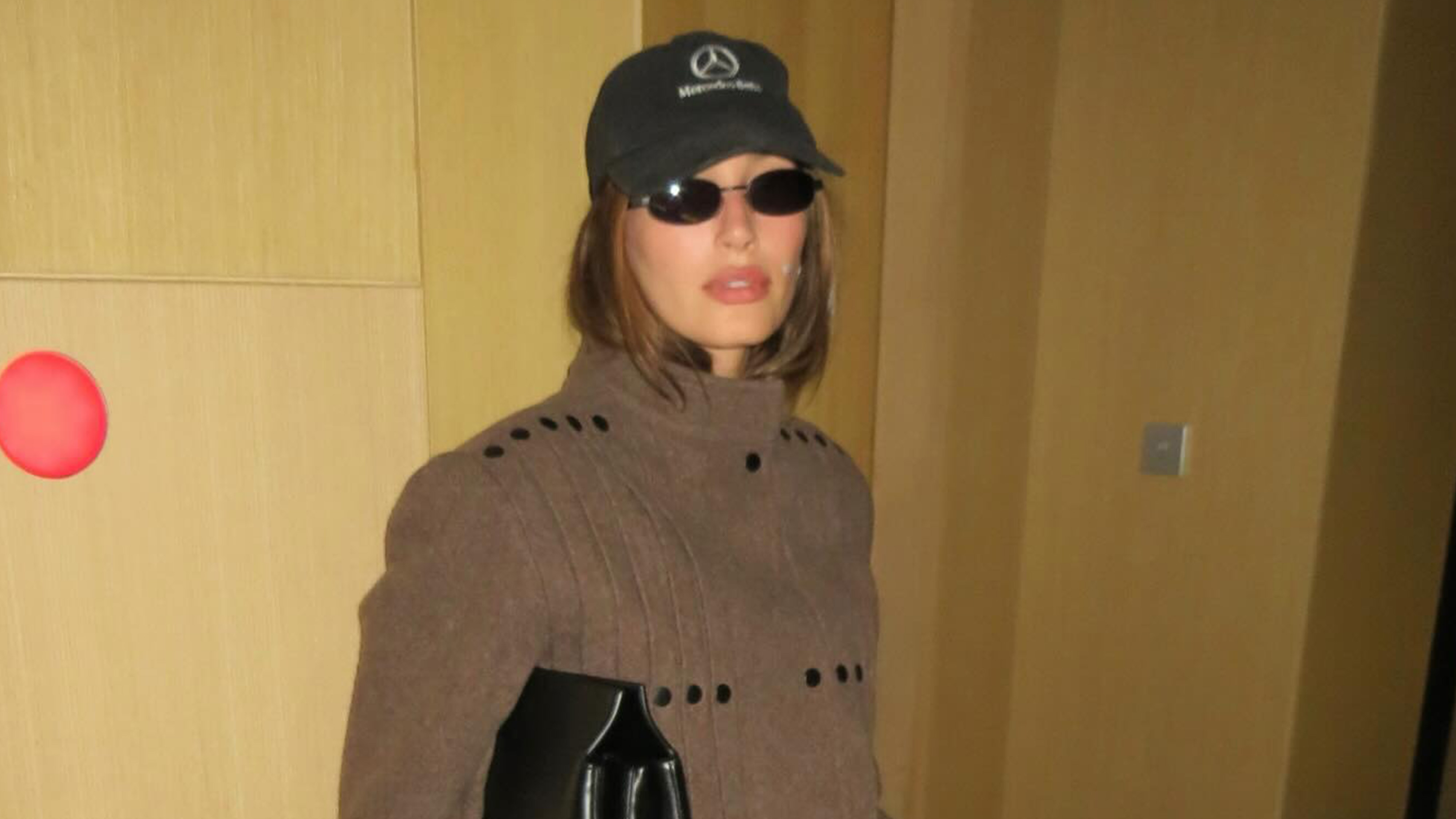 Hailey Bieber in Tokyo wearing a Mercedes baseball cap, brown jacket, and black leather pants.