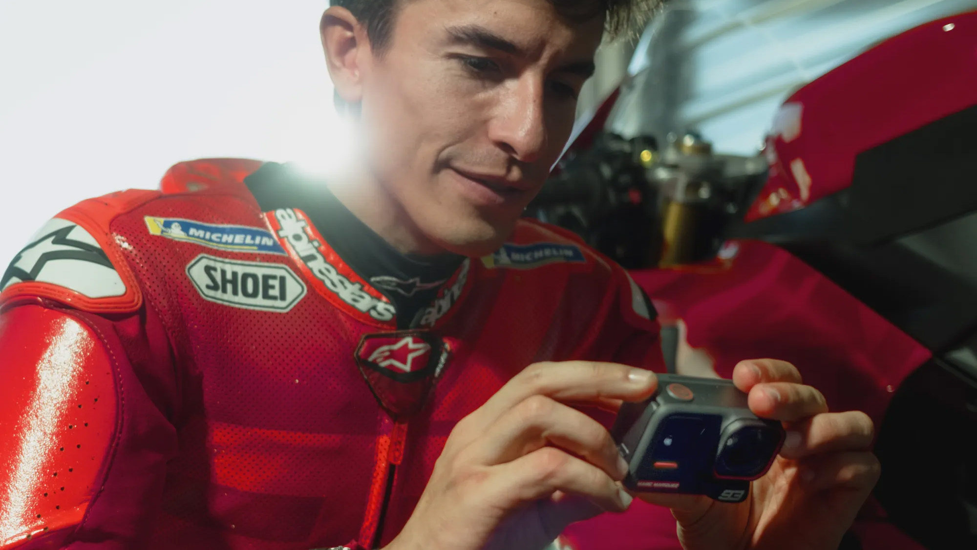 MotoGP champ Marc Márquez handling the Insta360 Ace Pro 2 MM93 Edition in a garage next to a Ducati motorbike 