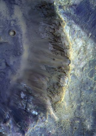 In this image, taken by the Color and Stereo Surface Imaging System (CaSSIS) onboard the European Space Agency's ExoMars Trace Gas Orbiter, shows the southeast wall of a small crater on Mars. The crater is found just about a couple hundred miles away from Hellas, a giant impact crater on the planet's surface. This smaller crater stretches about 7.5 miles (12 kilometers) across. The orbiter's photo shows a wide range of colors, which indicate the presence of different minerals in the planet's surface material.