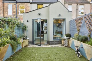 an exterior shot of the kitchen extension with angled roof and flower beds with blue painted triangles on the sides