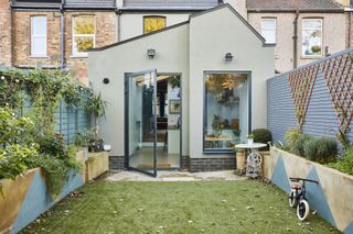 An exterior shot of the kitchen extension with angled roof and flower beds with blue painted triangles on the sides