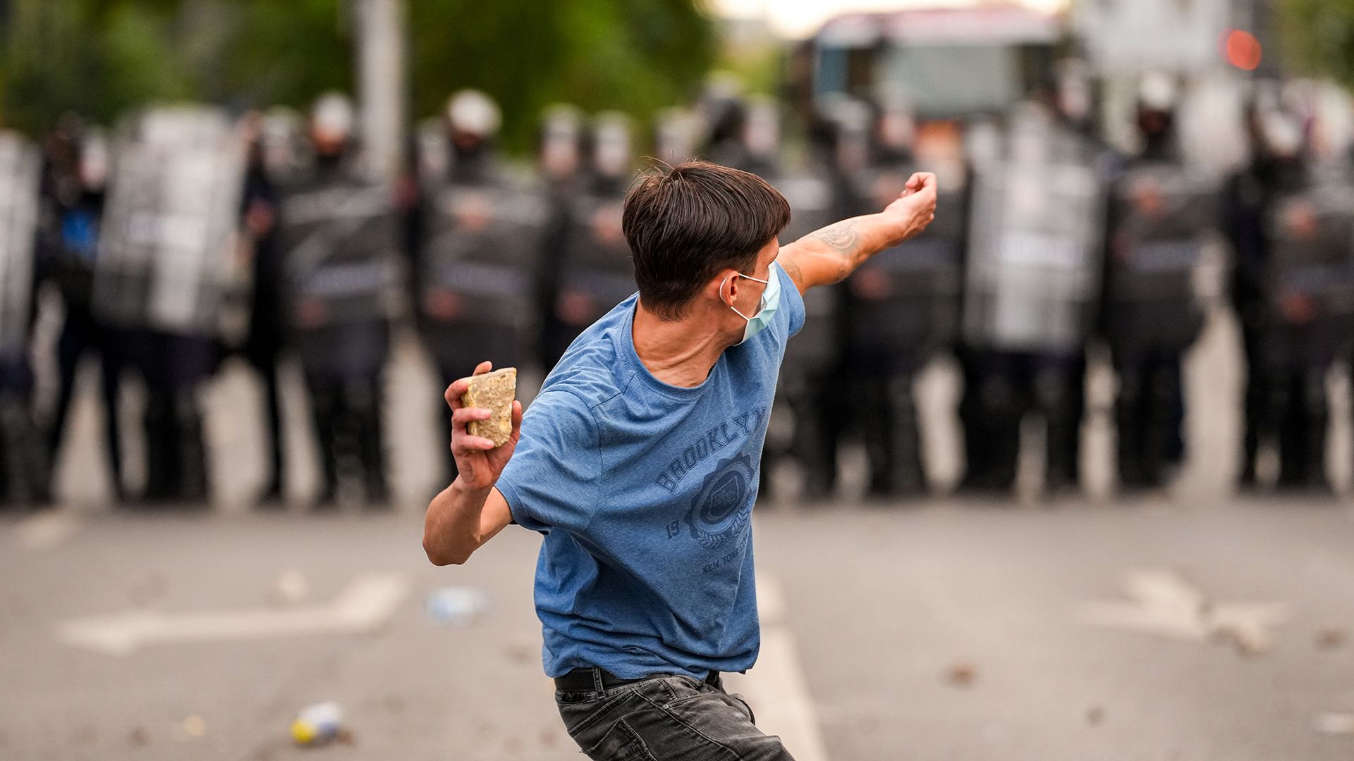 A demonstrator throws a rock towards a line of riot police during a farmers' protest in Bucharest, Romania