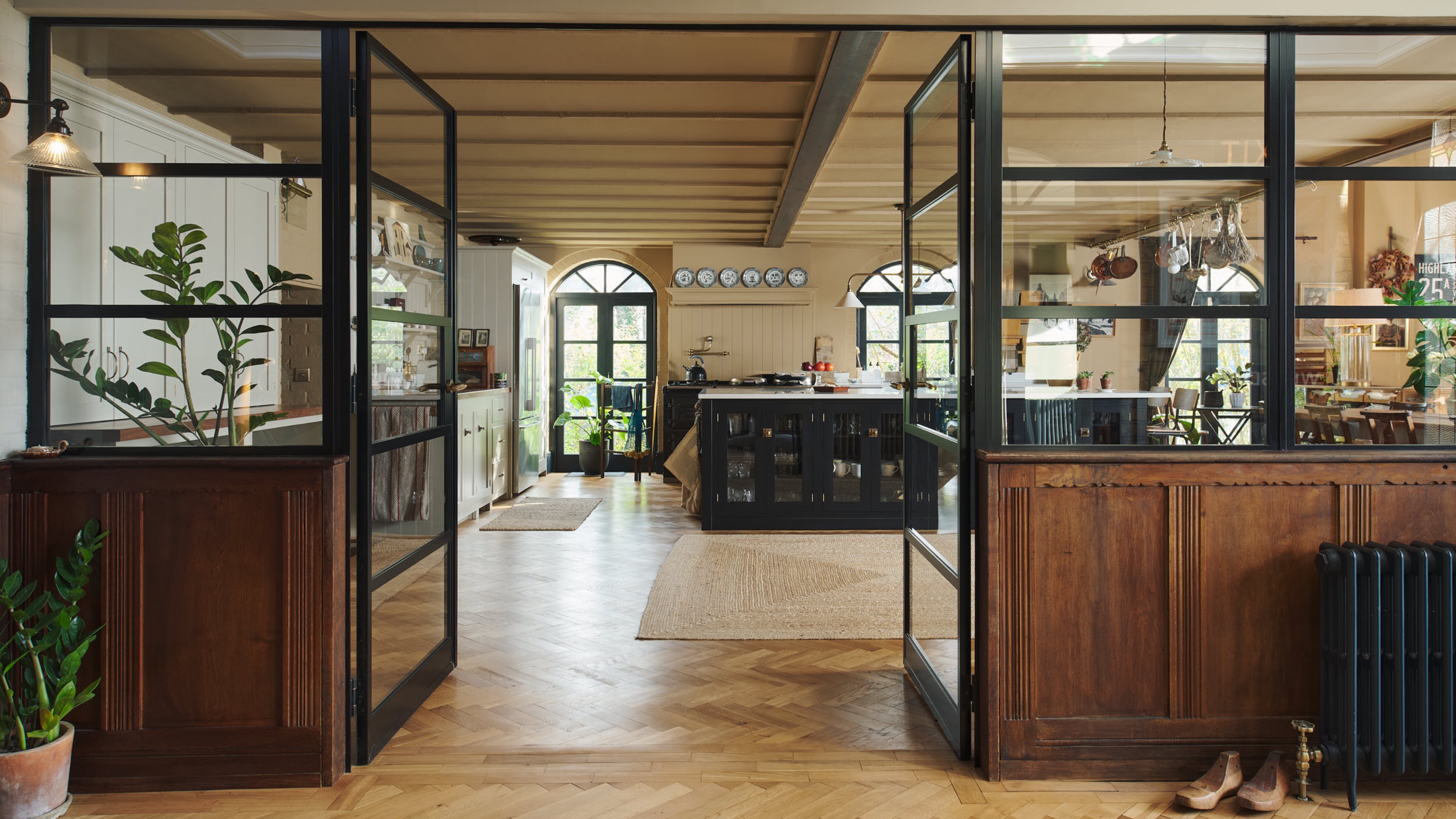 large kitchen with ochre walls, parquet flooring black kitchen island, white worktop, rugs, plates on shelf