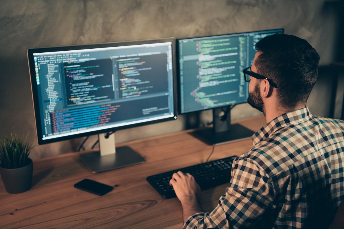 programmer sat in front of dual screens 