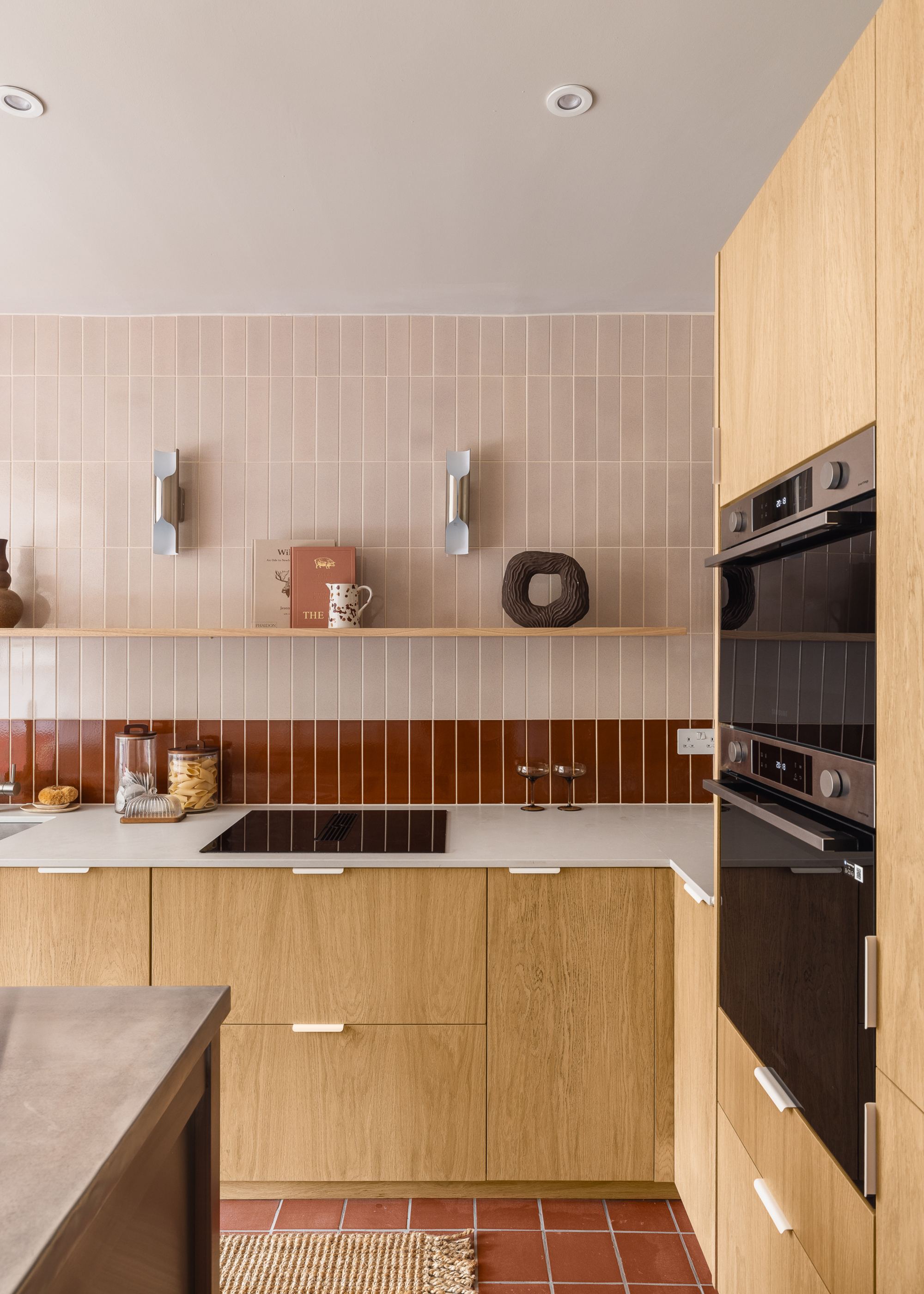 A kitchen made with IKEA base units, custom wooden cabinet fronts, a pink and red tiled wall, and terracotta tile flooring