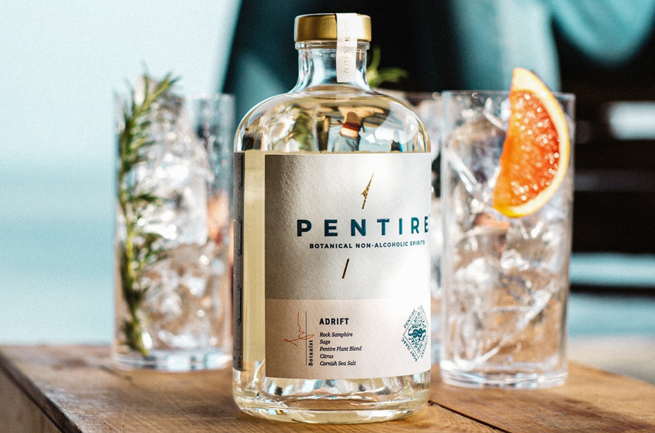 A clear bottle and glasses on a wooden table with the sea and a person in the background