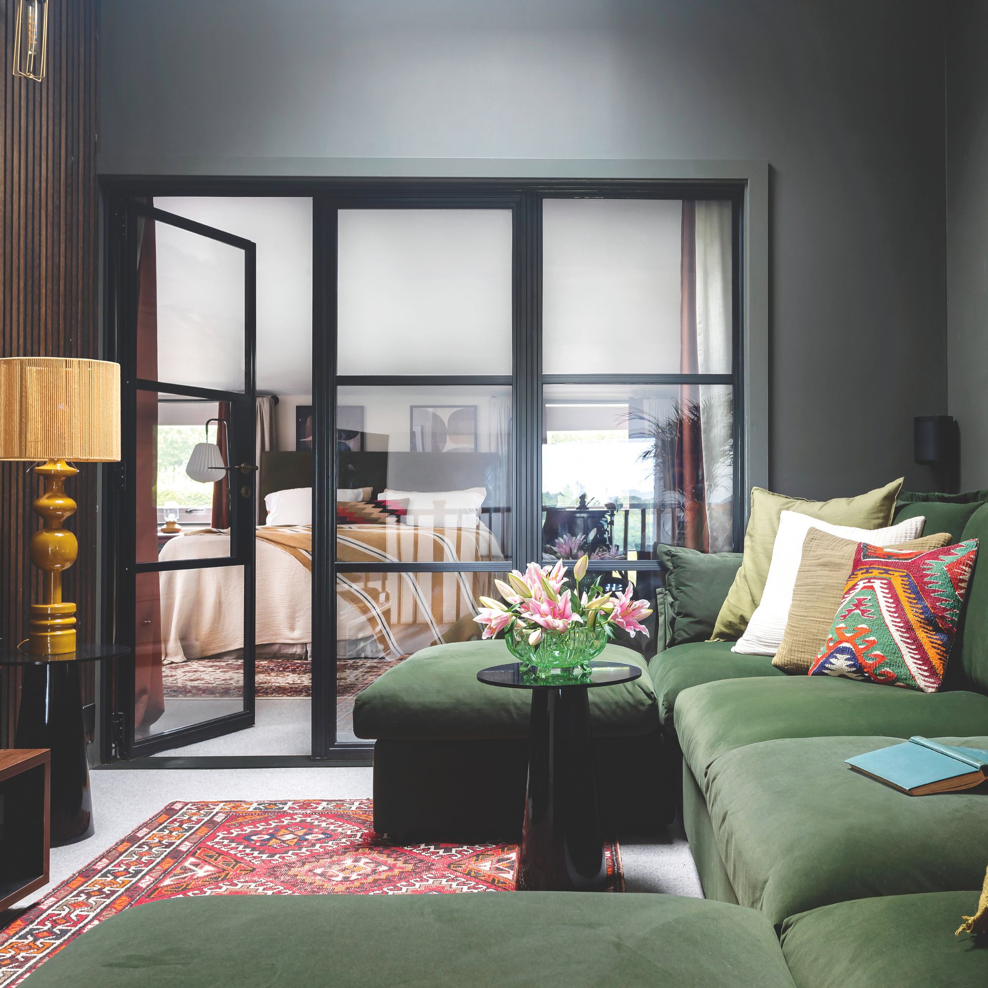 A snug room with black walls, a green velvet sofa and a red patterned rug