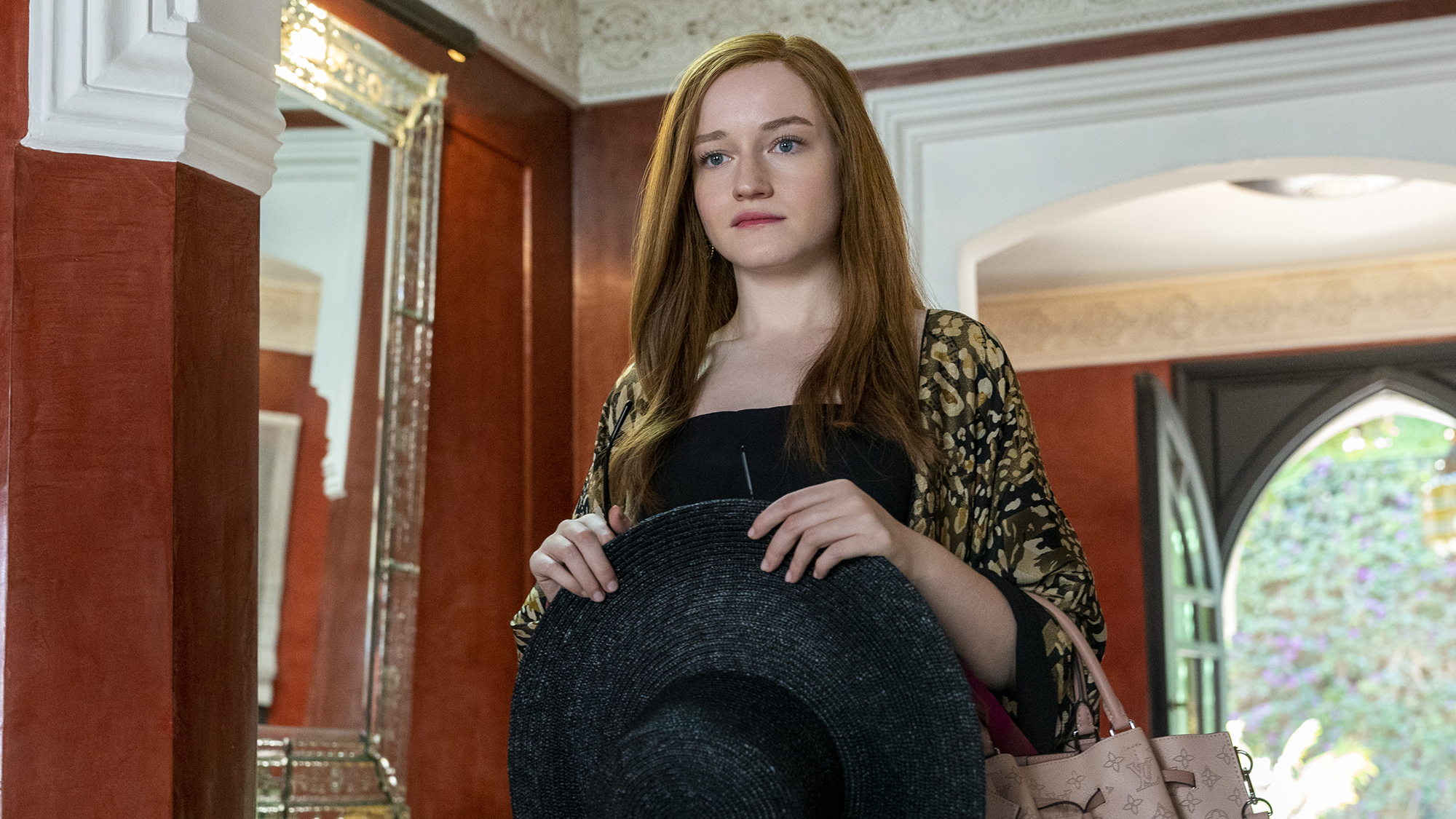 Julia Garner, as Anna Delvey, holding a wide-brim hat and a Louis Vuitton bag, in Inventing Anna