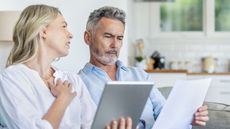 A serious couple work on financial planning together on their sofa.