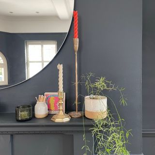 Detail of candles arranged on a black mantel with a round mirror behind and black wall