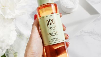 A woman&#039;s hand holding a bottle of pixi glow tonic for this pixi glow tonic review