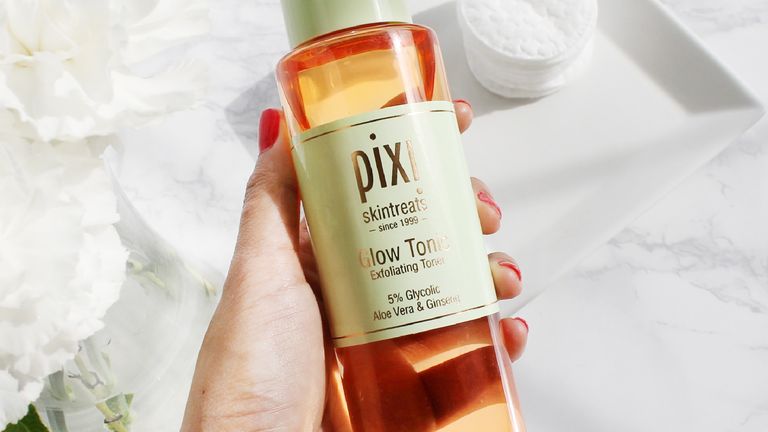 A woman's hand holding a bottle of pixi glow tonic for this pixi glow tonic review