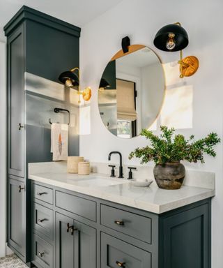 A bathroom with dark gray cabinets and a circular mirror over the sink